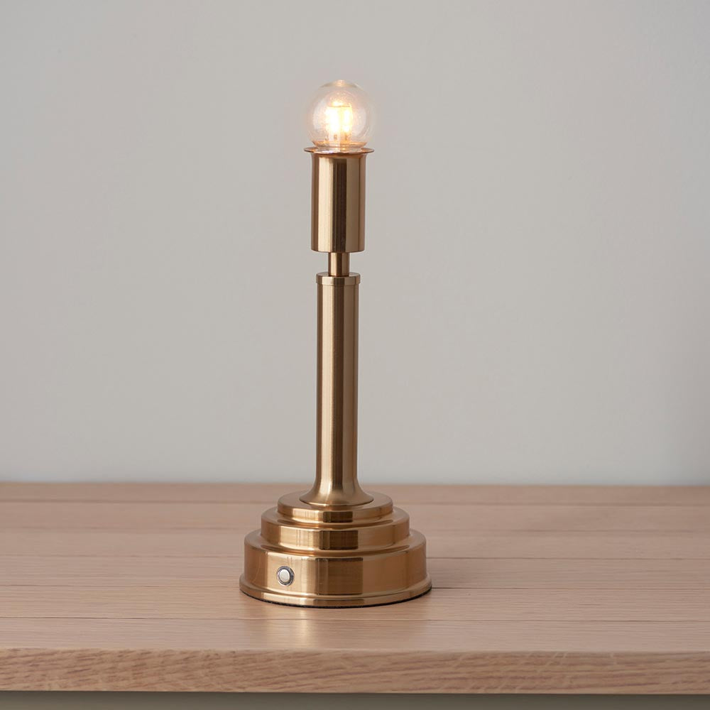 Danebourne brass stepped-column LED table lamp with exposed bulb, touch control, and no shade, on a wood surface against a plain light background.