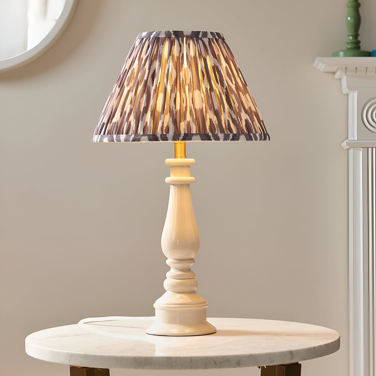 Carlworth Ikat Table Lamp in Grey, featuring a turned cream resin spindle base with a pleated grey Ikat-print fabric shade, shown lit on a marble side table.