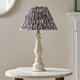 Carlworth Ikat Table Lamp with cream turned resin spindle base and pleated grey patterned fabric shade, shown on a marble side table in a living room.