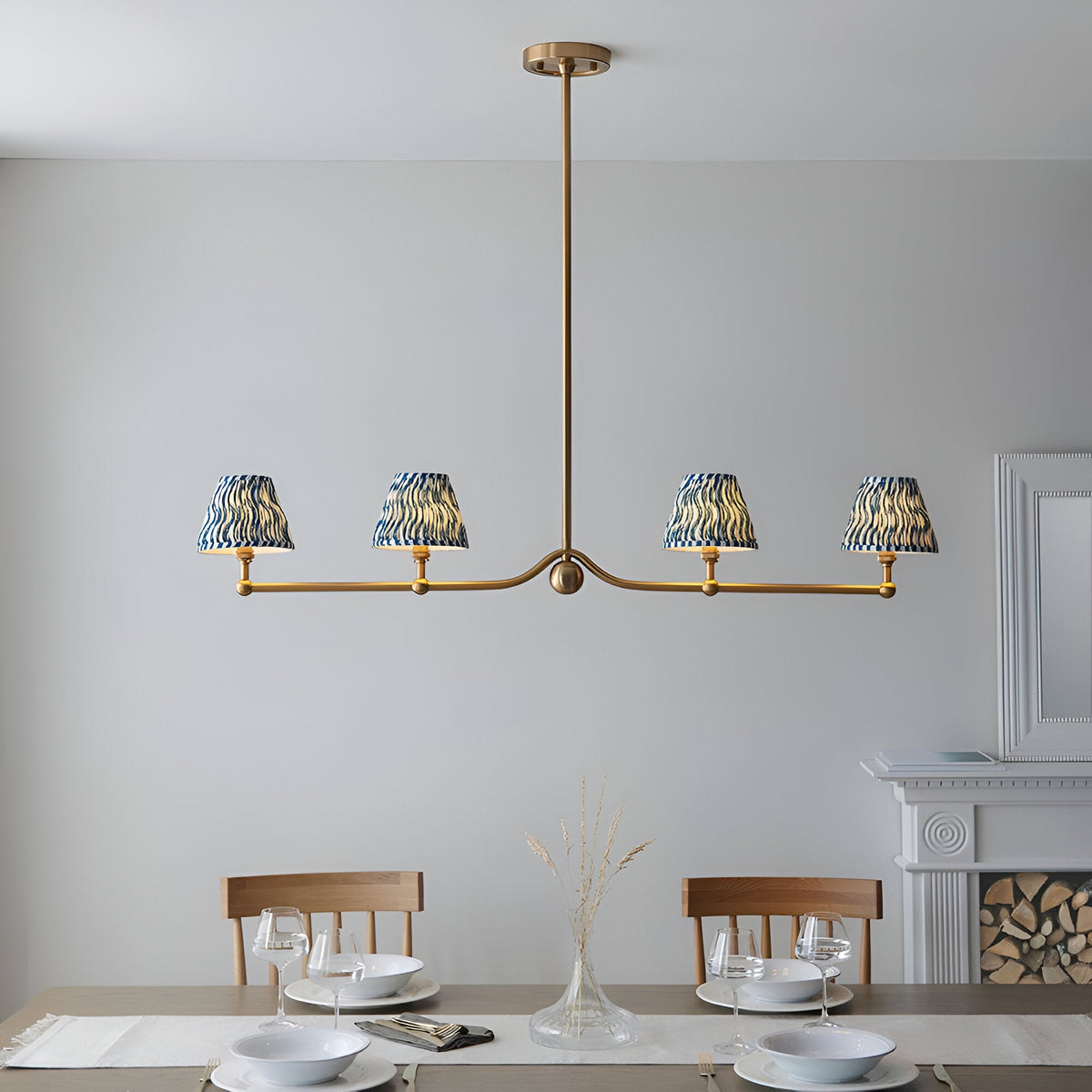 Cliffleigh 4 Light Ripple Pendant in brushed brass with blue patterned fabric shades, hung on a linear bar above a dining table in a light-walled room.