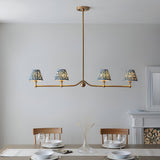 Cliffleigh 4 Light Ripple Pendant in brushed brass with blue patterned fabric shades, hung on a linear bar above a dining table in a light-walled room.