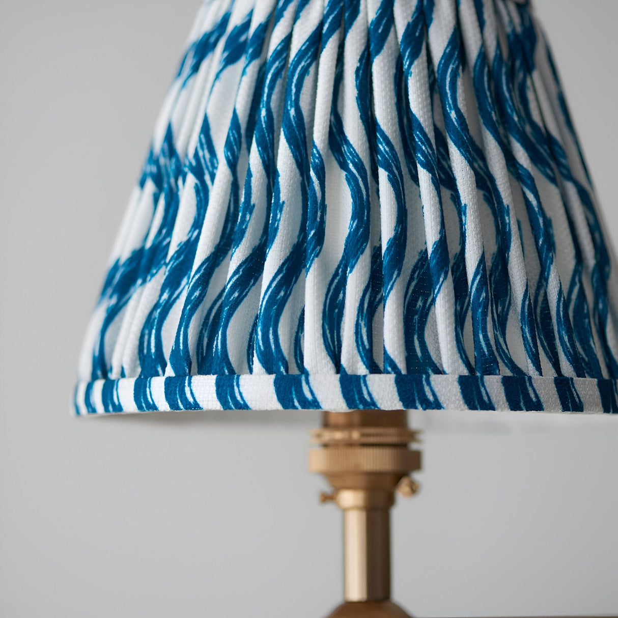 Close-up of the Cliffleigh 4 Light Ripple Pendant shade in blue wave-print pleated fabric with brass gallery fitting, against a plain light background.