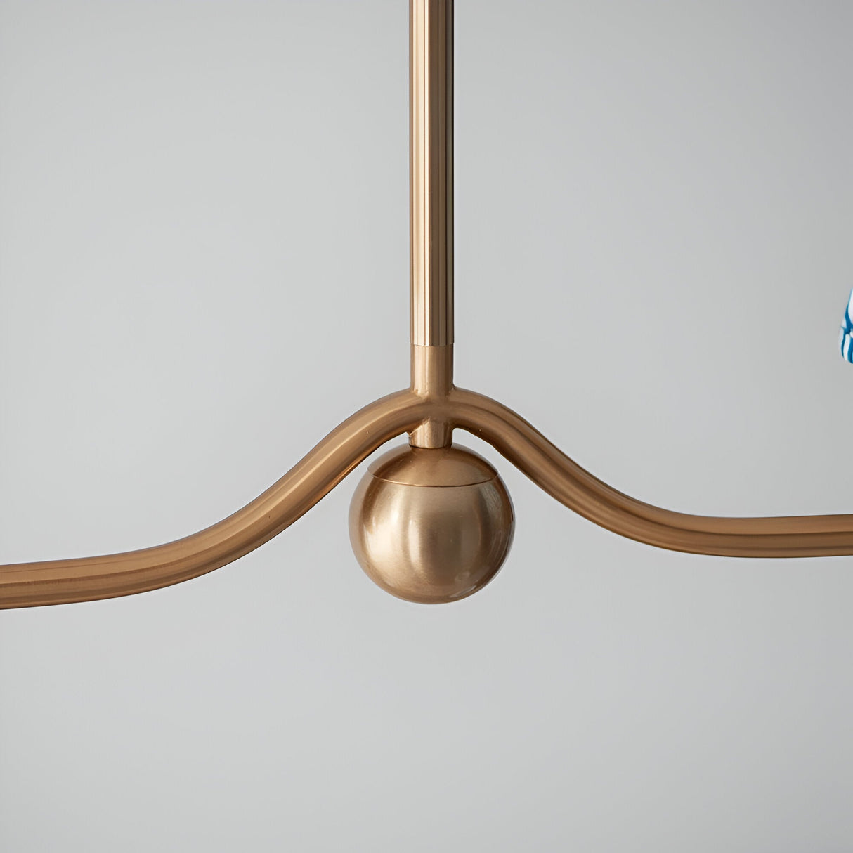 Cliffleigh 4 Light Ripple Pendant close-up in brushed antique brass, showing wave-shaped arms and central sphere detail against a plain light grey background.