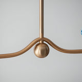 Cliffleigh 4 Light Ripple Pendant close-up in brushed antique brass, showing wave-shaped arms and central sphere detail against a plain light grey background.
