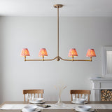 Endon Cliffleigh 4 light linear pendant in brushed aged brass with four coral pink pleated ikat taper shades, shown above a dining table.