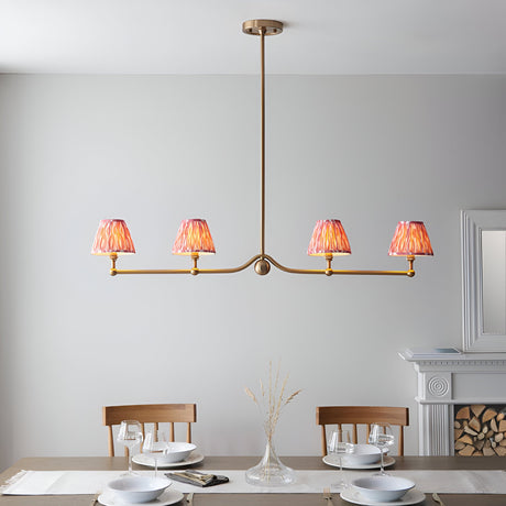 Endon Cliffleigh 4 light linear pendant in brushed aged brass with four coral pink pleated ikat taper shades, shown above a dining table.