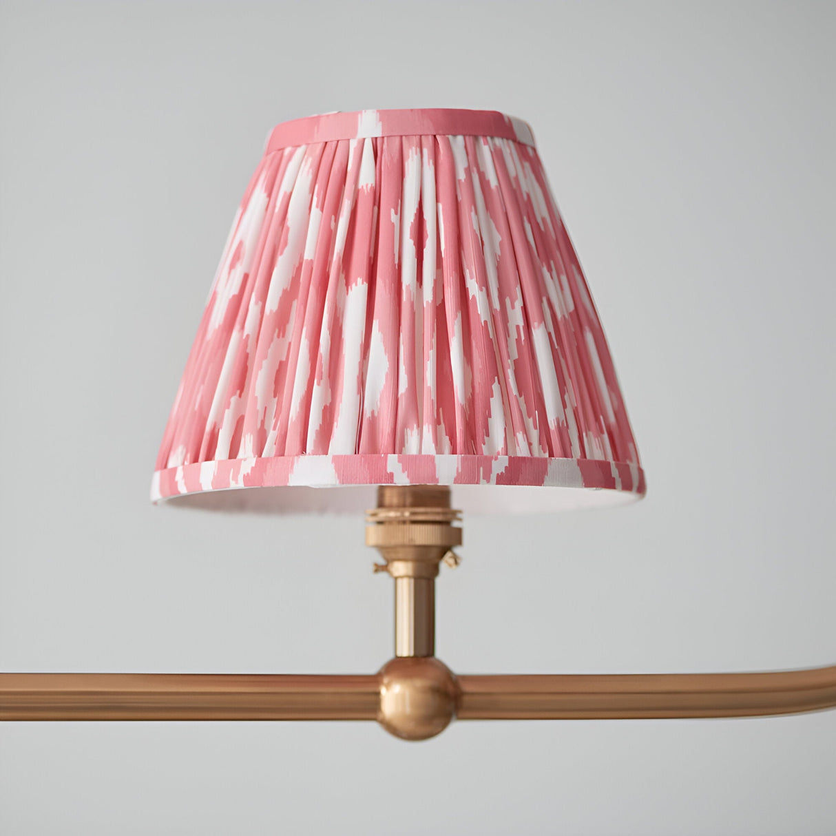 Close-up of one coral pink ikat pleated faux silk tapered shade on the Endon Cliffleigh pendant, mounted to a brushed aged brass arm with sphere detail.