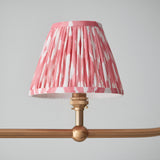 Close-up of one coral pink ikat pleated faux silk tapered shade on the Endon Cliffleigh pendant, mounted to a brushed aged brass arm with sphere detail.