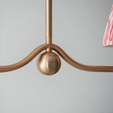 Close-up of Endon Cliffleigh pendant showing brushed aged brass curved bar with sphere detail and edge of a coral pink pleated faux silk shade.