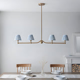 Endon Cliffleigh Leaf 4 light linear pendant in brushed brass with four tapered blue leaf-print shades, above a dining table by a fireplace.