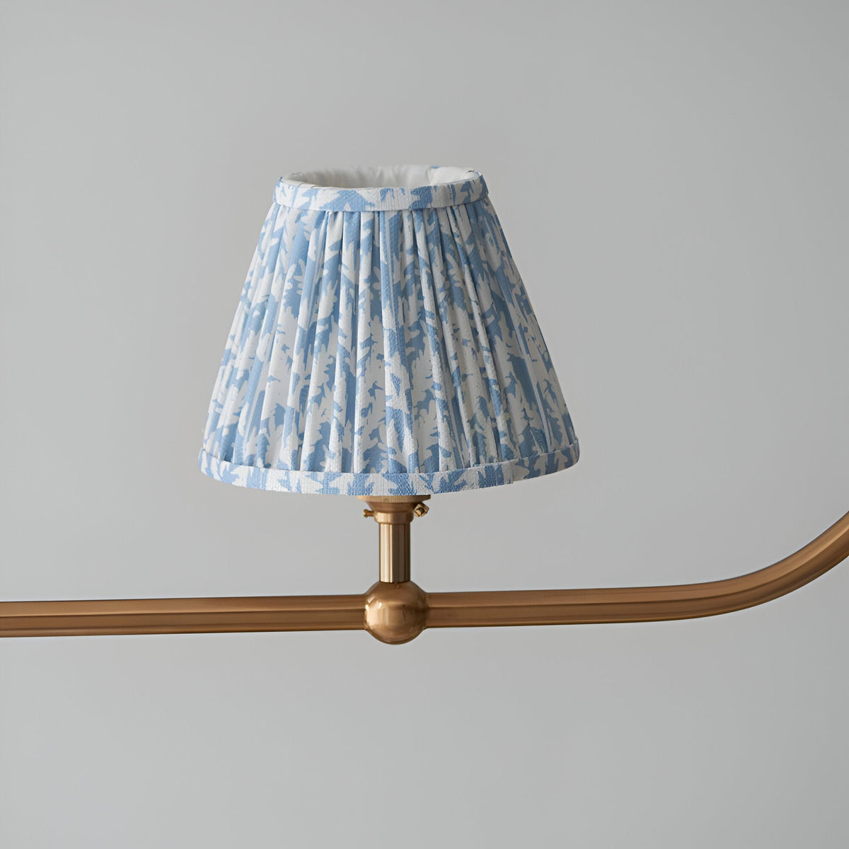 Close-up of one pleated blue Leaf-print tapered shade on the Endon Cliffleigh linear pendant's brushed aged brass bar with sphere detail.