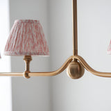 Close-up of the Cliffleigh Leaf 4 Light Linear Pendant in brushed brass, showing a pink patterned tapered shade and sphere detail on the curved bar.