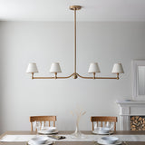 Endon Cliffleigh 4 light linear pendant in brushed aged brass with white tapered fabric shades, hung above a dining table by a fireplace.