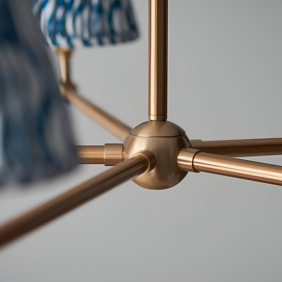 Close-up of the Cliffleigh 5 Light Ripple Pendant's brushed aged brass frame, showing the central hub with radiating arms and blue pleated fabric shades.