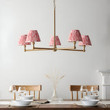 Endon Cliffleigh Ikat 5 light pendant in brushed brass with pink Ikat pleated tapered shades, shown above a wooden dining table set with glassware.