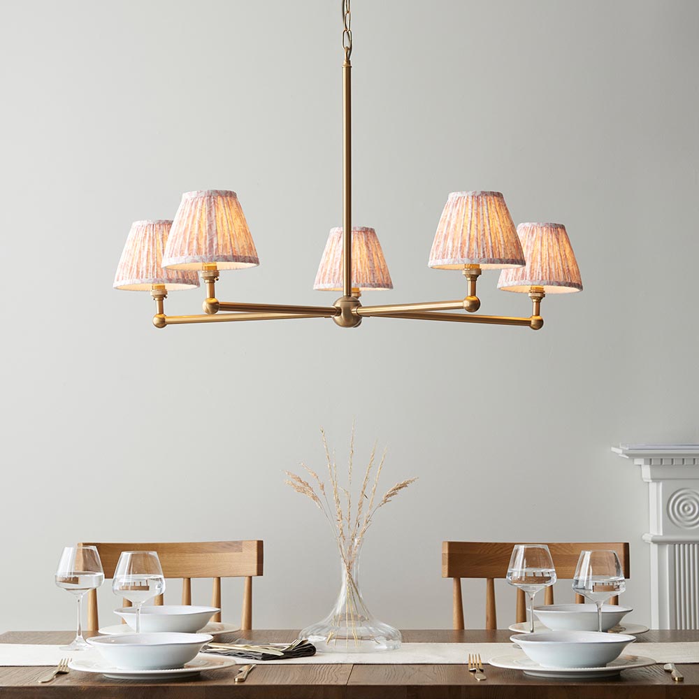 Cliffleigh Leaf 5 Light Pendant in brushed brass with five pleated fabric shades, hung above a dining table in a light grey room setting.