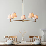 Cliffleigh Leaf 5 Light Pendant in brushed brass with five pleated fabric shades, hung above a dining table in a light grey room setting.
