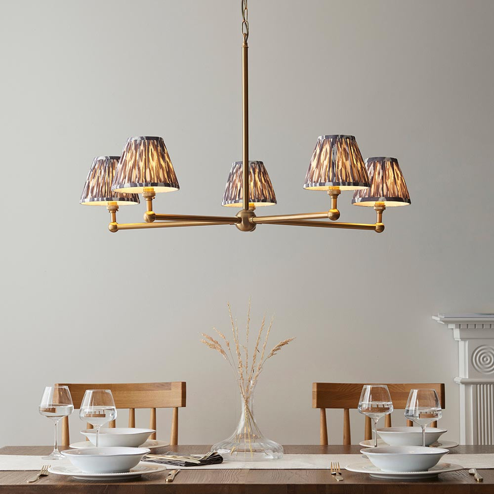 Cliffleigh Ikat 5 Light Pendant with brushed brass frame and pleated grey Ikat-patterned shades, shown above a dining table in a neutral room setting.