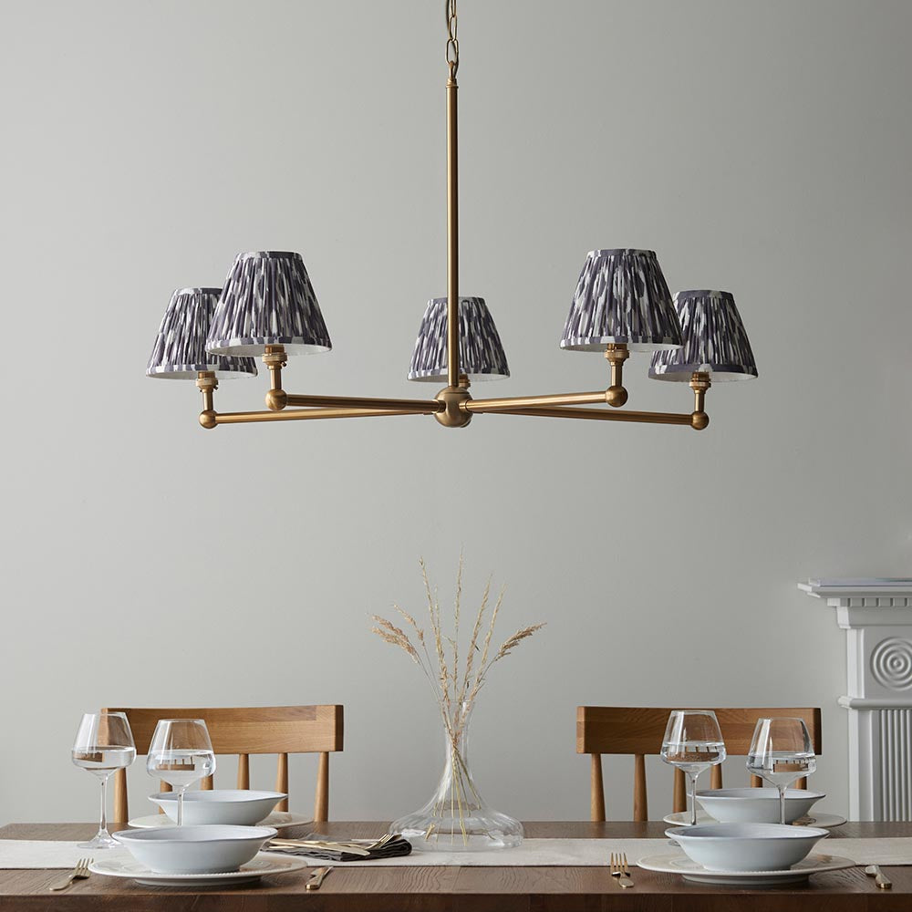 Cliffleigh Ikat 5 Light Pendant in brushed brass with pleated grey Ikat fabric shades, shown above a dining table in a light-toned room.