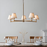 Endon Cliffleigh 5 light pendant in brushed aged brass with white tapered fabric shades, hung above a wooden dining table set with glassware.