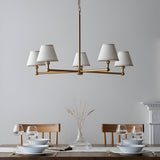 Endon Cliffleigh 5 light pendant in brushed aged brass with white tapered fabric shades, hung above a wooden dining table set for two.