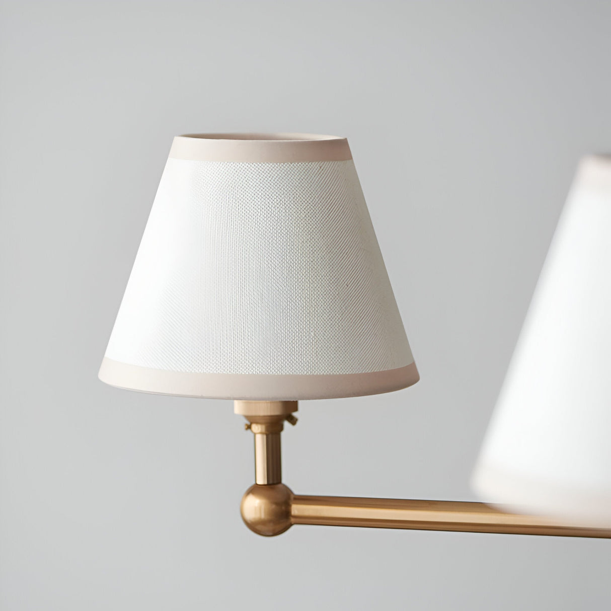 Close-up of an Endon Cliffleigh pendant shade in vintage white cotton mix with almond taped edges, mounted on a brushed aged brass arm.