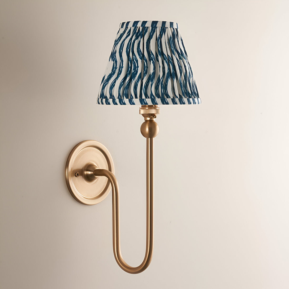 Endon Cliffleigh Ripple wall light in brushed aged brass with a pleated marlin blue faux linen tapered shade, mounted on a plain wall.