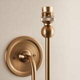 Close-up of the Endon Cliffleigh wall light's brushed brass B22 lamp holder, ball detail and round flat back plate against a pale wall.