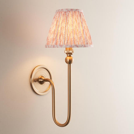 Endon Cliffleigh Leaf Wall Light II in brass, a curved single-arm wall light with a pleated peach leaf-print tapered fabric shade on a neutral wall.