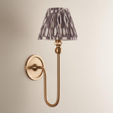 Cliffleigh Ikat Wall Light with brushed brass swan-neck arm and pleated grey and cream patterned fabric shade, mounted on a plain wall backplate.