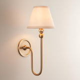 Cliffleigh Ivy brushed aged brass wall light with tapered vintage white fabric shade, curved arm and round wall back, on a plain light background.