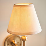 Cliffleigh Ivy Wall Light in vintage white, tapered fabric shade with taped edge on a brushed aged brass backplate, close-up view.
