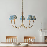 Endon Cliffleigh 5 light curved-arm pendant in brushed aged brass with marlin blue rippled fabric shades, hung above a dining table by a fireplace.