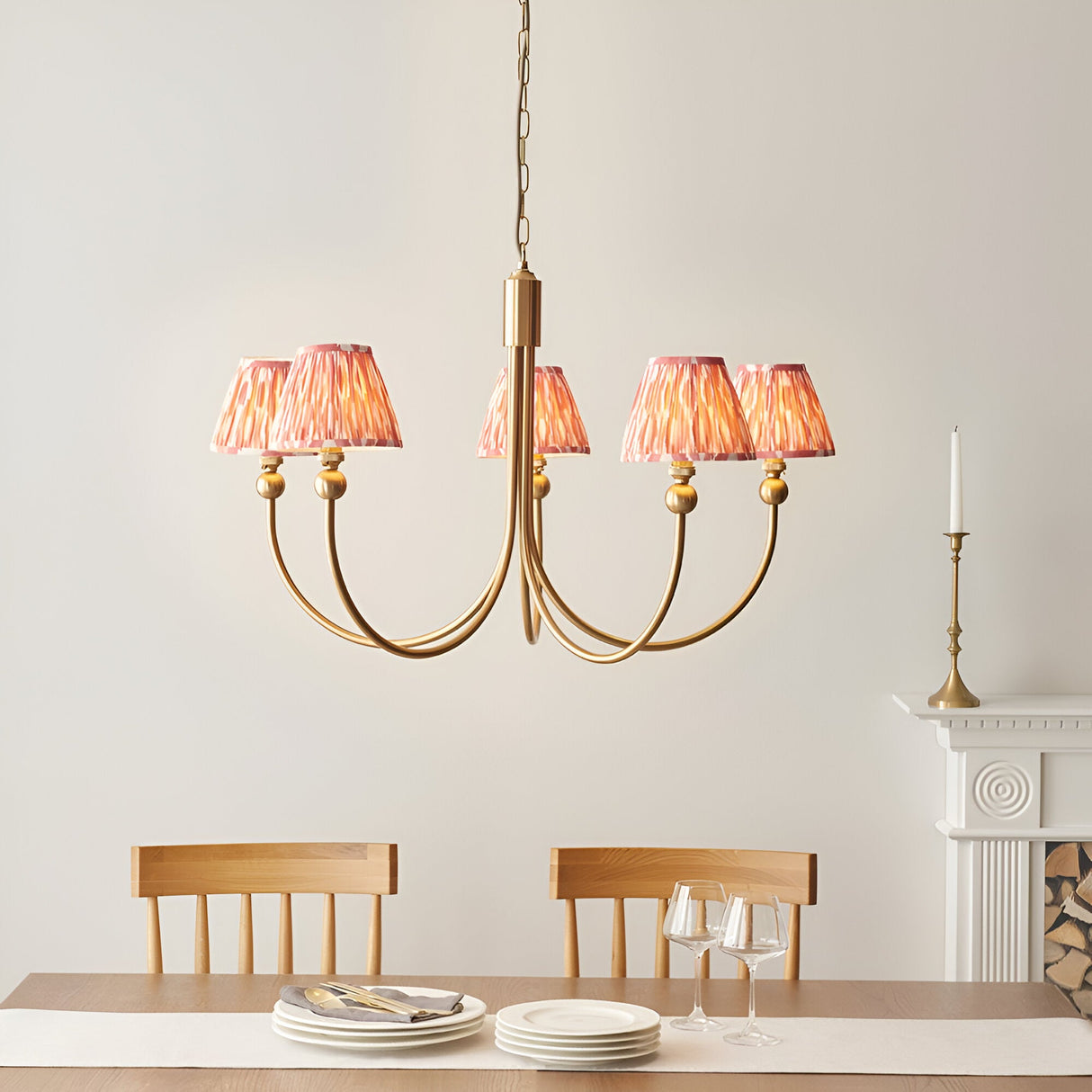 Cliffleigh 5-Light Curved Arm Ikat Pendant in Coral with brushed aged brass frame and pleated fabric shades, above a dining table with wooden chairs.
