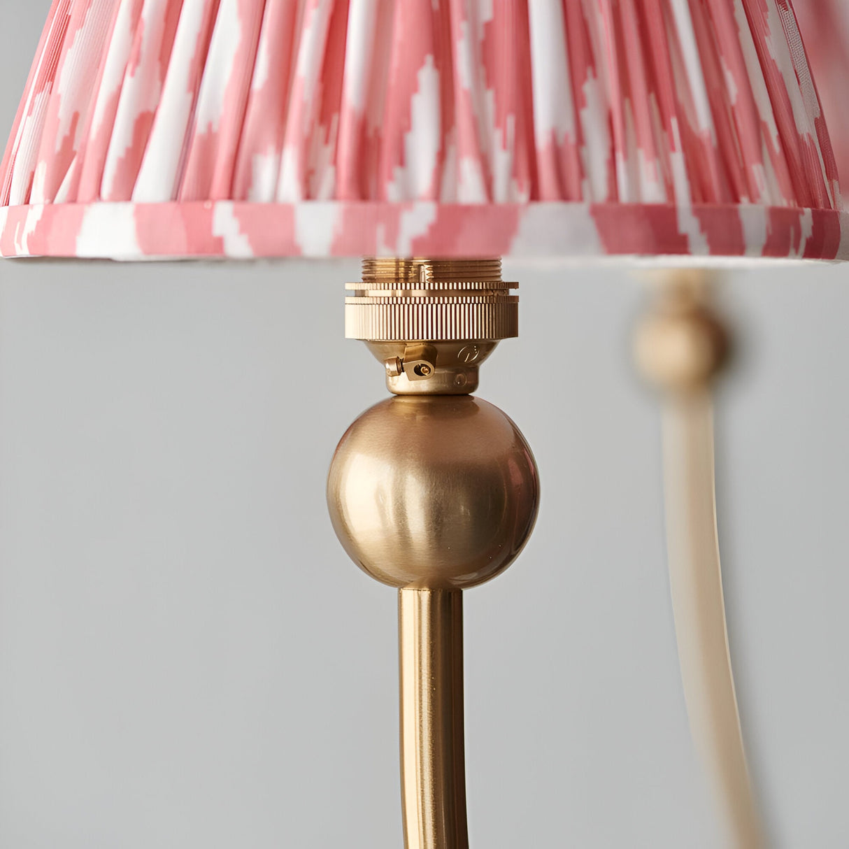 Close-up of the Cliffleigh 5 Light Curved Arm Ikat Pendant in coral, showing a brushed brass gimbal fitting and pleated coral-and-white shade.