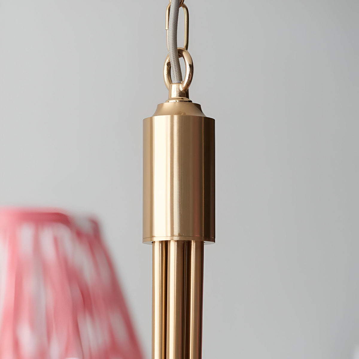 Close-up of the Cliffleigh 5-Light pendant's brushed aged brass frame, chain hook, and curved arms, with a blurred coral fabric shade.
