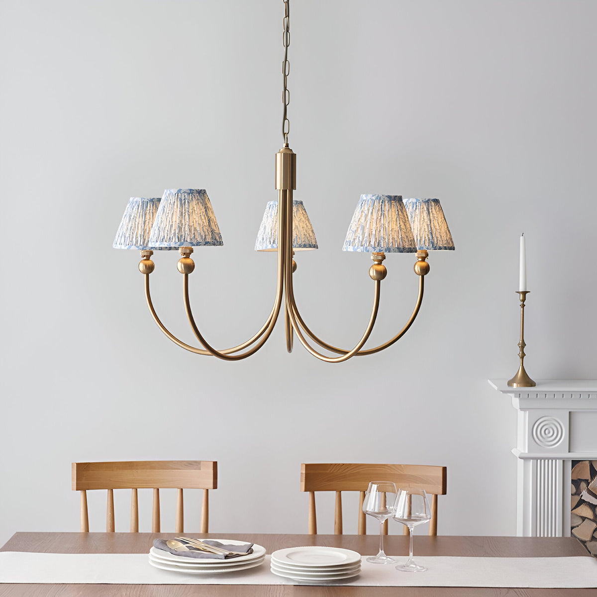 Endon Cliffleigh Leaf 5 light pendant with curved brushed brass arms and tapered blue leaf-print fabric shades, above a dining table by a fireplace.