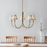 Endon Cliffleigh Leaf 5 light pendant with curved brushed brass arms and tapered blue leaf-print fabric shades, above a dining table by a fireplace.