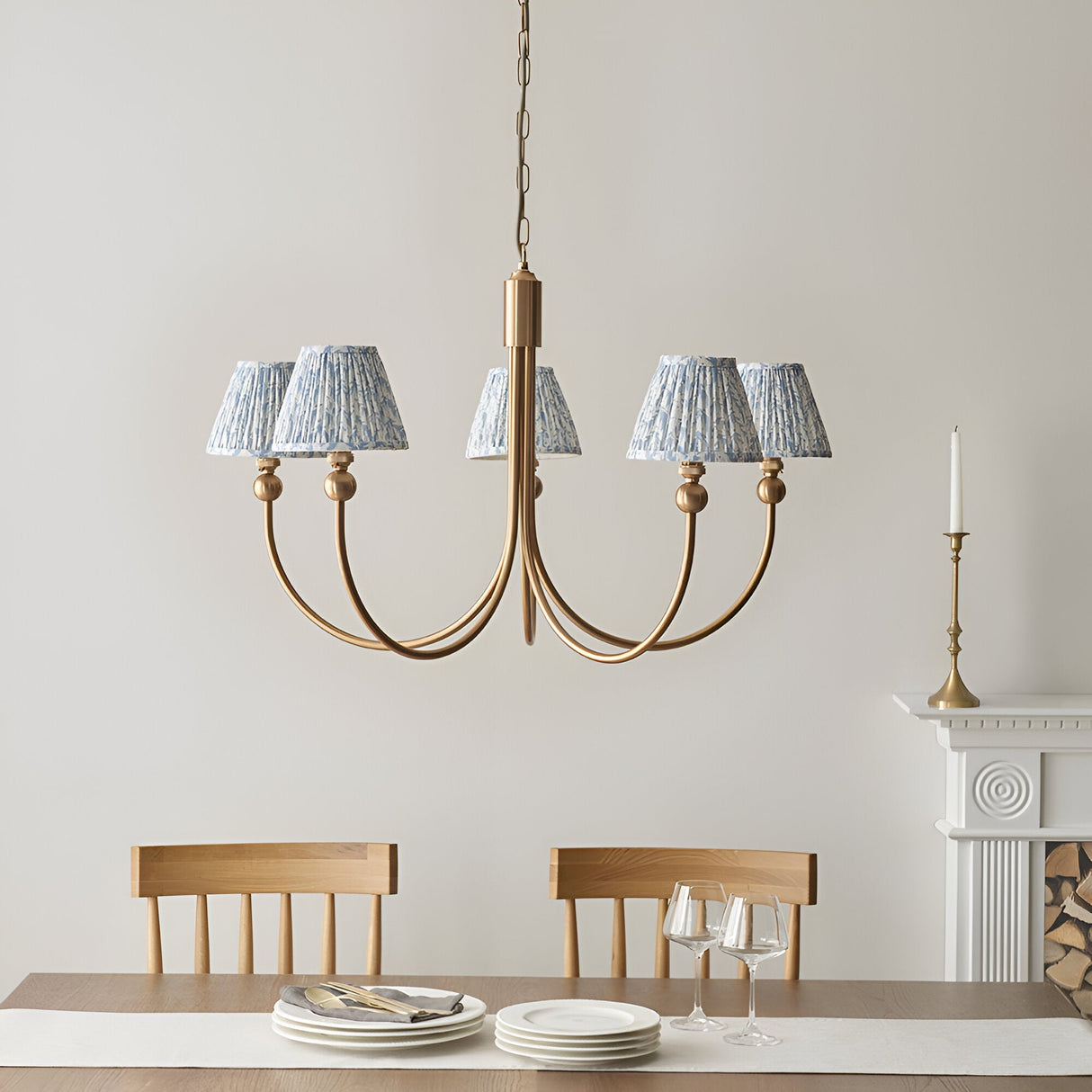 Endon Cliffleigh Leaf five-light curved-arm pendant in brushed brass with blue leaf-print tapered shades, above a dining table beside a fireplace.