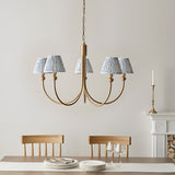 Endon Cliffleigh Leaf five-light curved-arm pendant in brushed brass with blue leaf-print tapered shades, above a dining table beside a fireplace.