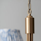 Close-up of the Endon Cliffleigh Leaf pendant's brushed aged brass ceiling chain and cylindrical fitting, with a blue Leaf-print shade softly blurred below.