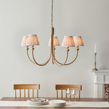 Cliffleigh Leaf 5 Light Curved Arm Pendant with brass finish and pleated grey Leaf-pattern shades, hung above a dining table in a neutral room.