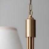 Close-up of the Cliffleigh pendant light's brushed brass ceiling hook and chain, with a tapered white fabric shade edge visible against a grey background.