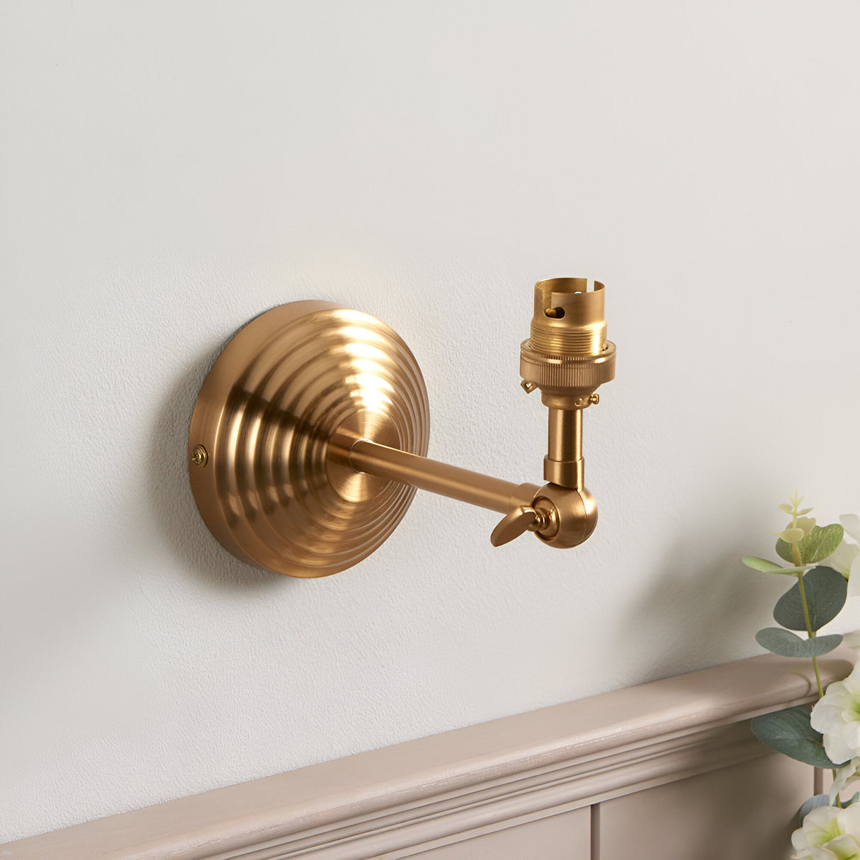 Endon Castley wall light in brushed aged brass with stepped back plate, linear arm, adjustable knuckle and B22 lampholder, mounted above a moulded shelf.