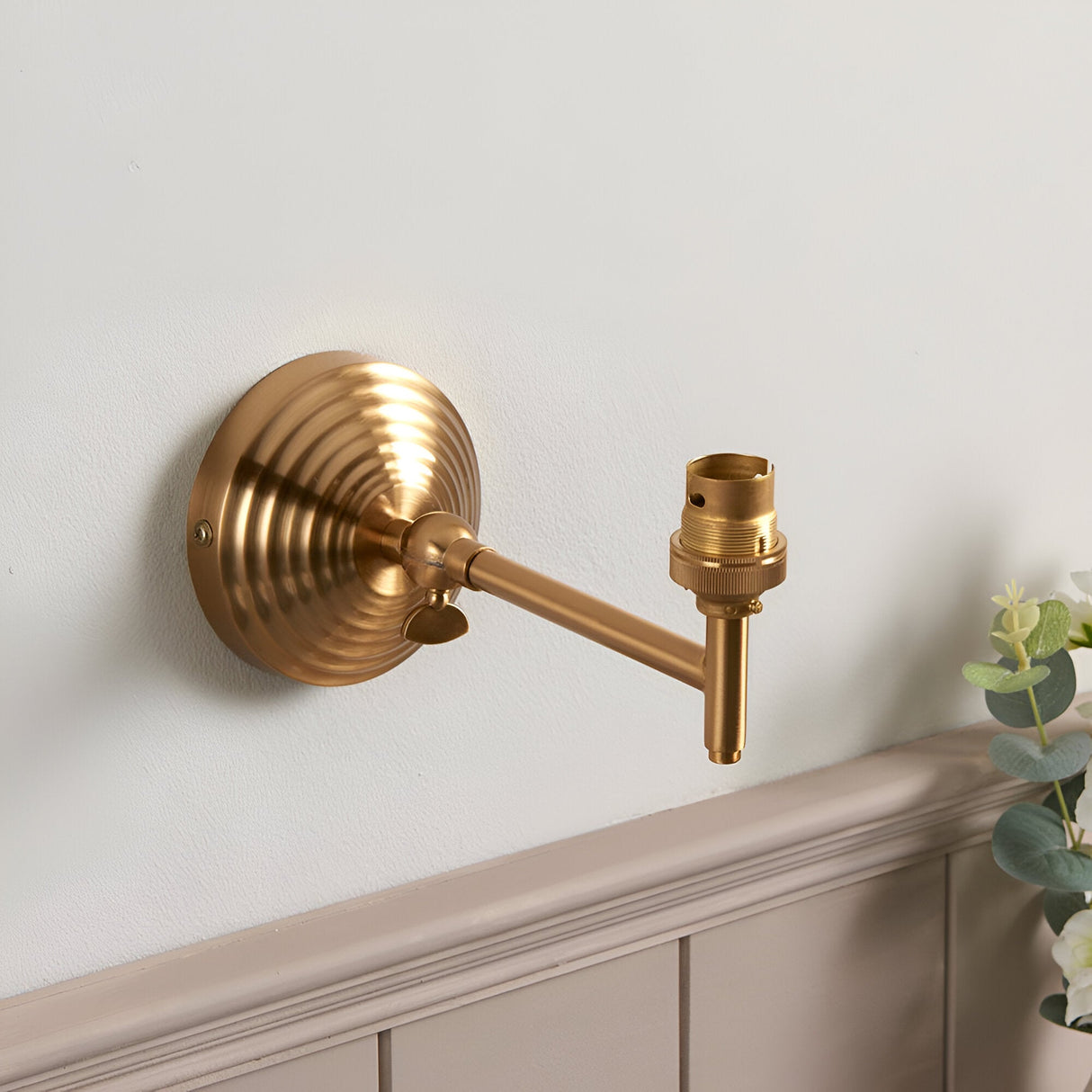 Endon Casthurst wall light in brushed aged brass with a stepped back plate, adjustable knuckle, linear arm, and B22 lampholder, mounted above panelling.
