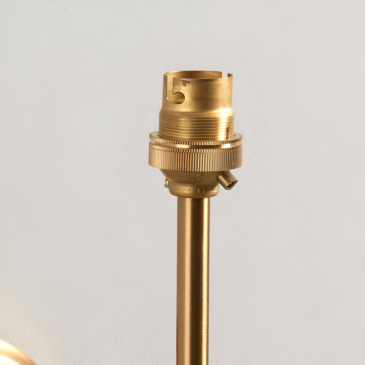 Close-up of the Endon Castleigh wall light's brushed aged brass B22 lampholder and slim stem against a pale wall.