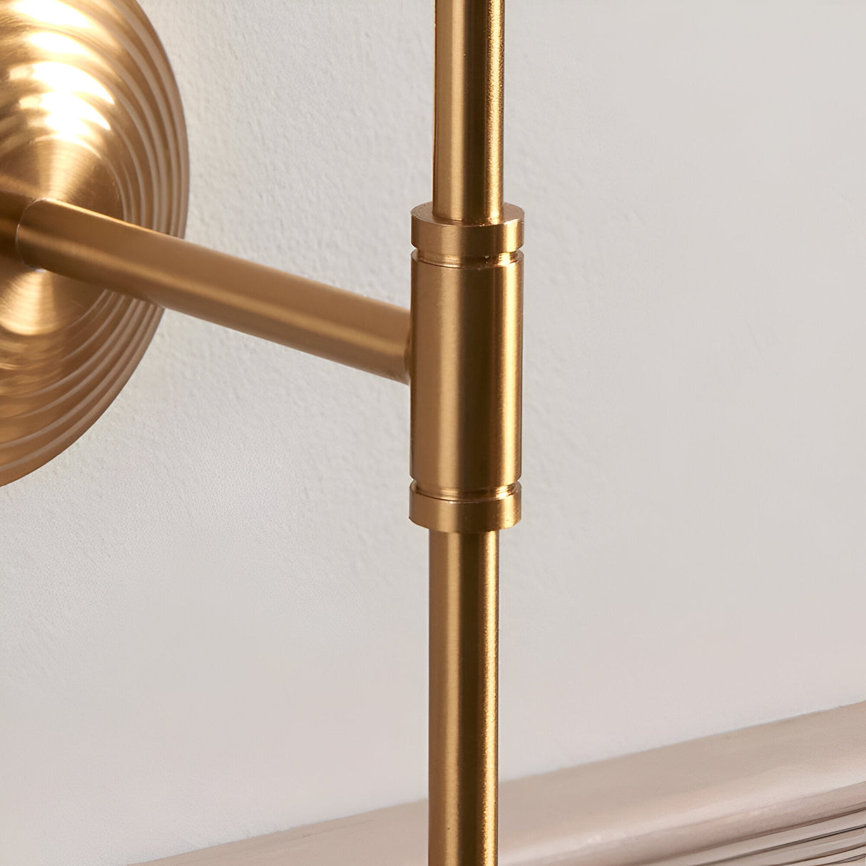 Close-up of the Endon Castleigh wall light showing the brushed aged brass T-bar arm, stepped backplate, and cylindrical joint against a white wall.
