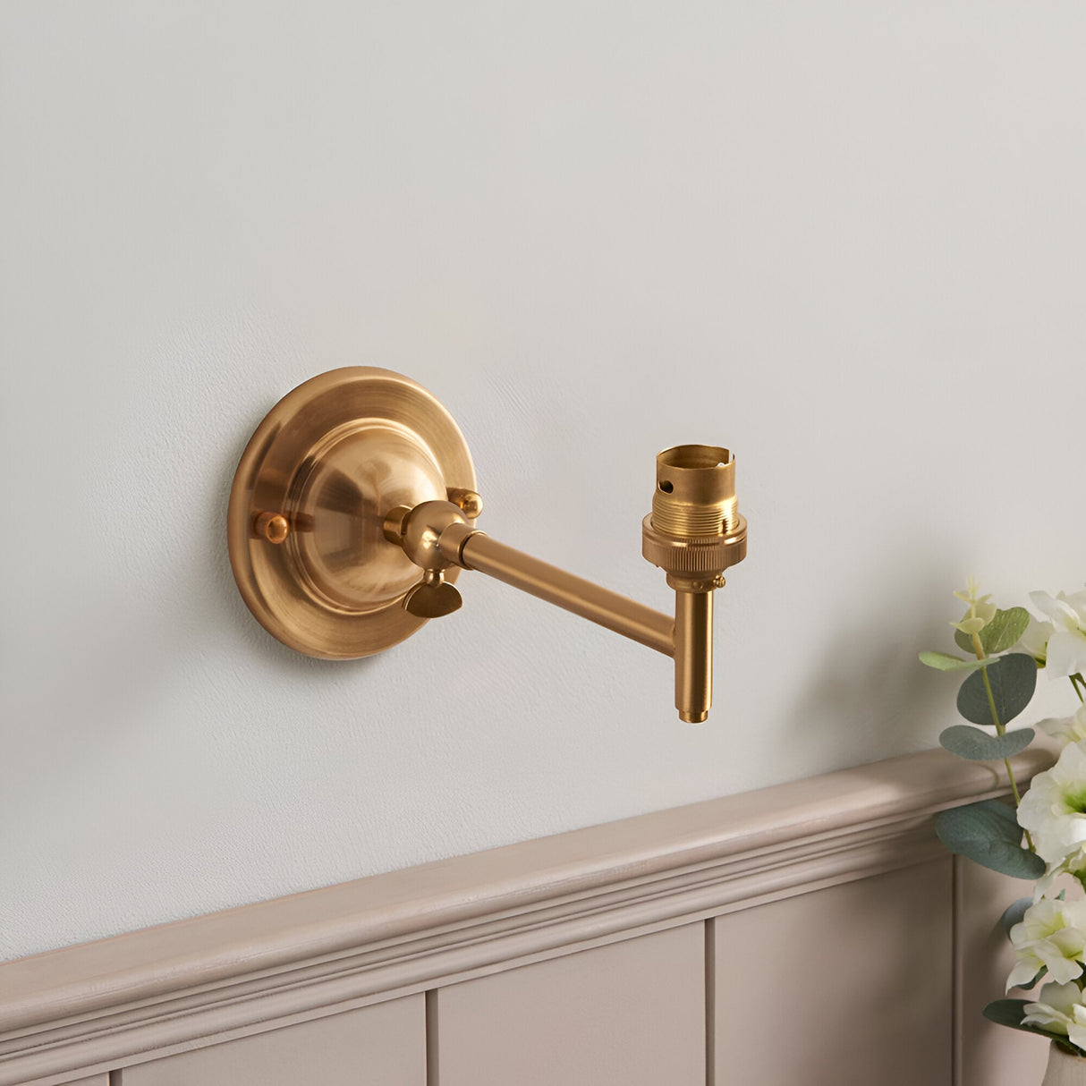 Endon Brackdon wall light in brushed aged brass with a rounded dome backplate, adjustable knuckle arm and B22 lampholder, mounted above panelled wainscoting.