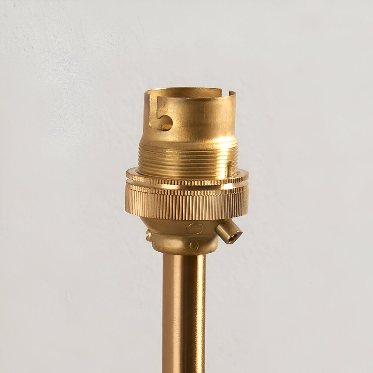 Close-up of the Endon Brackfield Wall Light's brushed aged brass B22 lampholder and knurled shade ring atop a slim arm against a plain white wall.