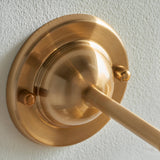 Close-up of the Endon Brackfield wall light's brushed aged brass domed backplate with fixing knobs and T-bar arm mounted on a white wall.